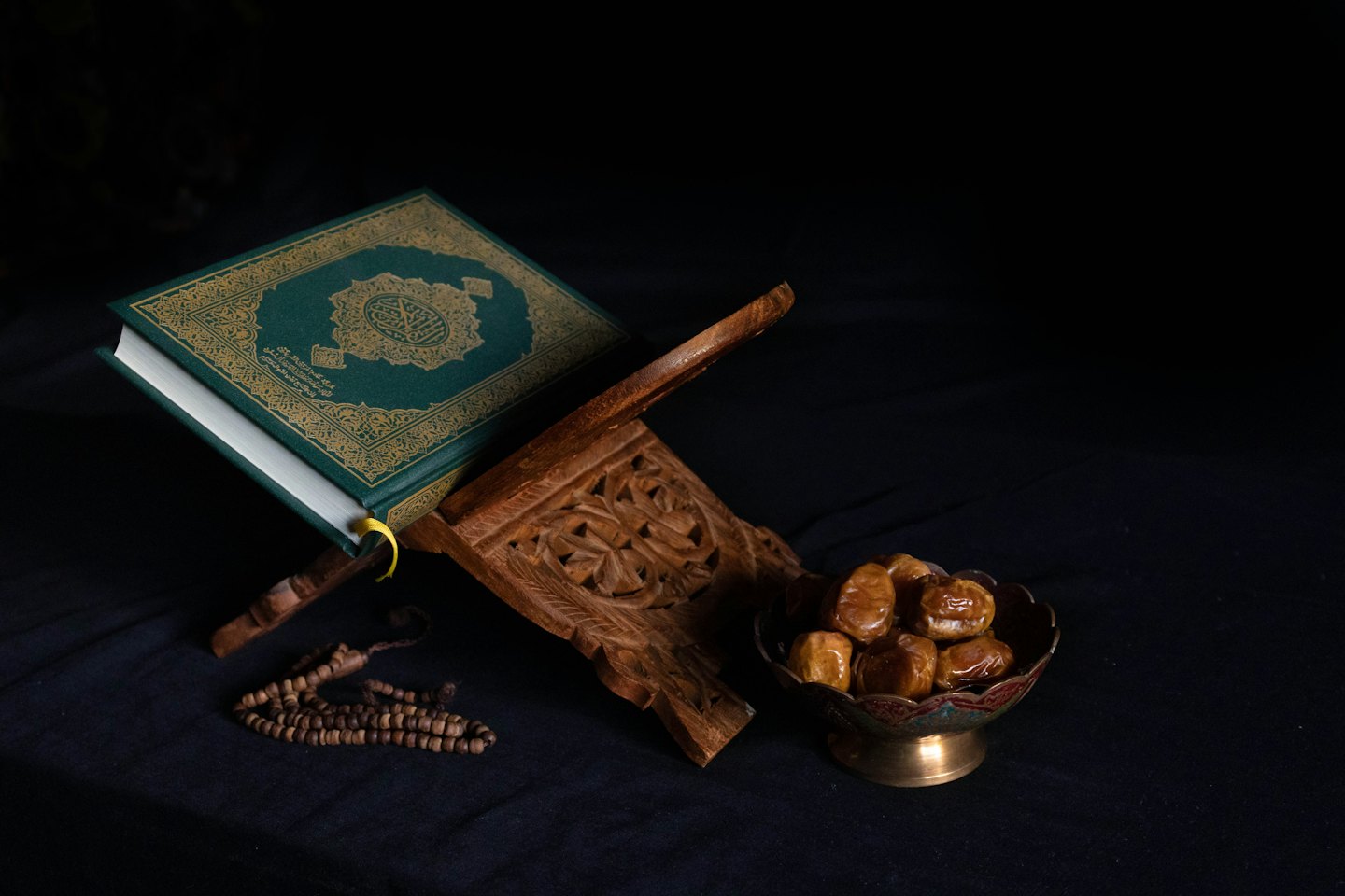 Quran on a wooden stand with prayer beads and dates.