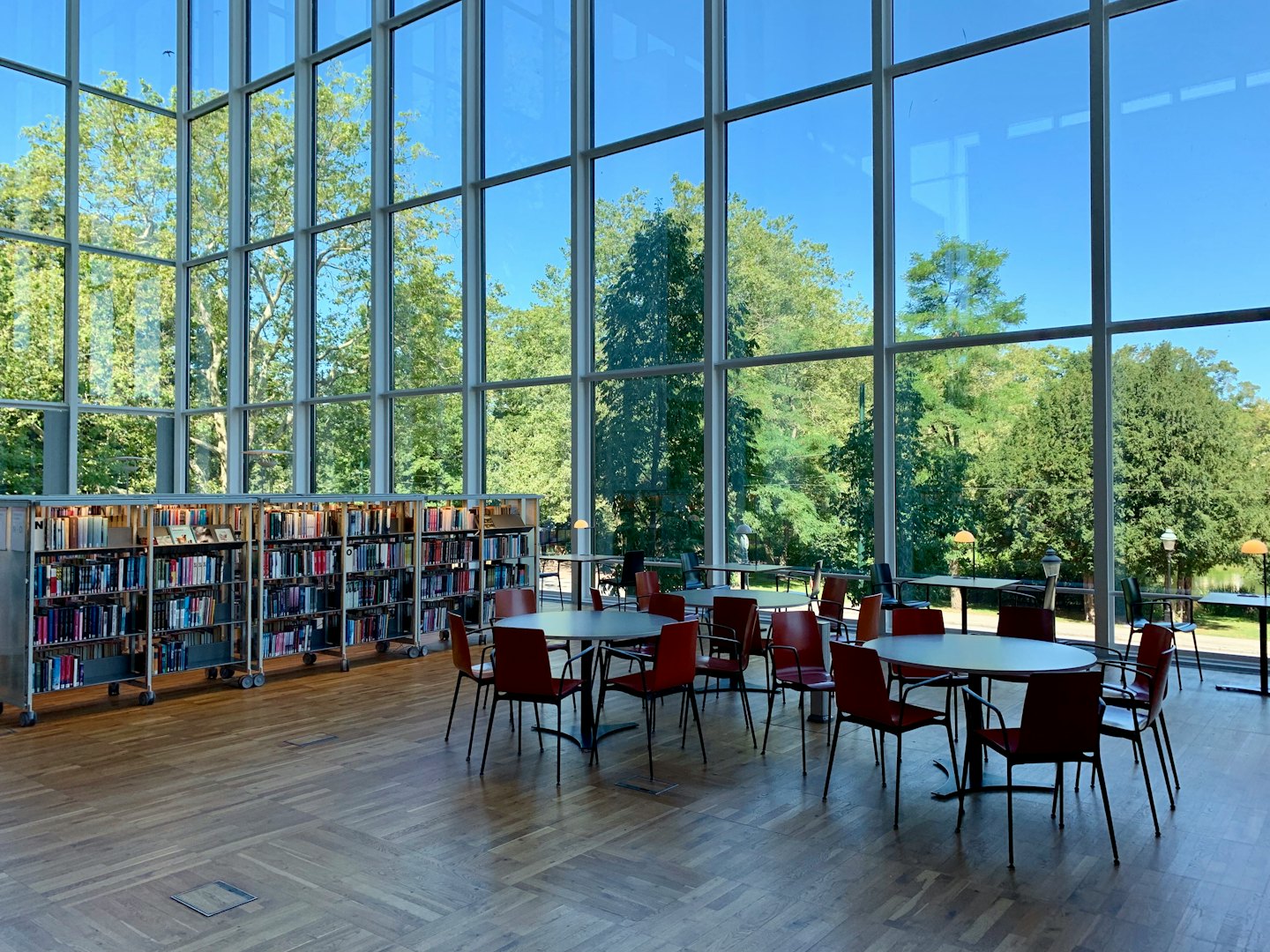 Modern library with book trolleys and round tables by large windows.